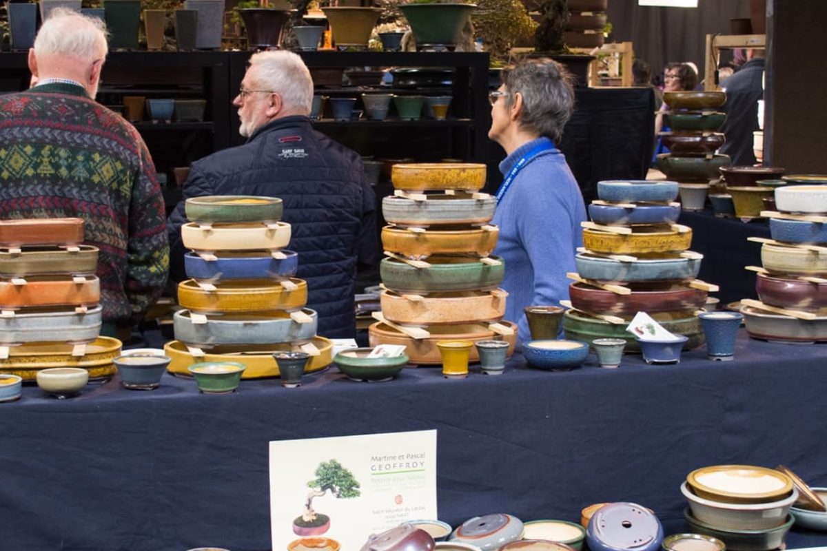 Un stand de poteries à bonsaï, pots empilés devant des visiteurs
